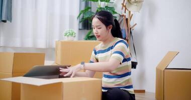 Handheld selective focus shot, Young Asian woman pack belongings into cardboard boxes and wrapping with duct tape in preparation for moving into new house. Moving house and lifestyle concept. video