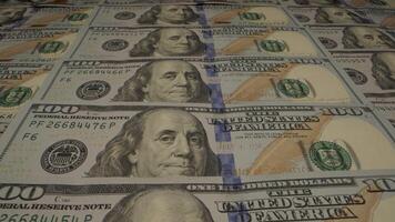 A close-up shot of a stack of one hundred dollar bills, showing the portrait of Benjamin Franklin and the details of the currency. Moving camera video