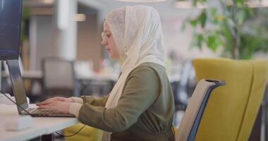 A businesswoman in a hijab is seen working on a computer in a modern office, highlighting inclusivity and professionalism in a diverse workplace video