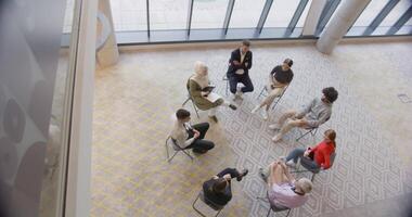 Top view of a diverse group of young business entrepreneurs gathered in a circle for a meeting, discussing corporate challenges and innovative solutions within the modern confines of a large video