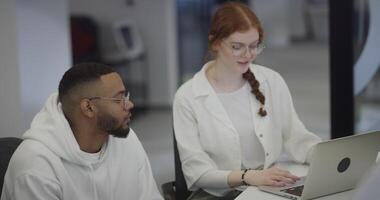 A woman with vibrant orange hair and an African-American business man work together in a modern office, collaboratively solving various business challenges, illustrating diversity, innovation, and video