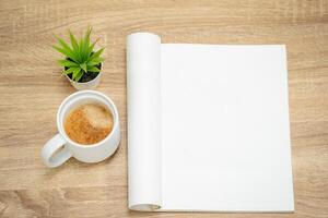 Glass of hot coffee with an open empty magazine on a wooden table or desk from above in mock up concept. photo