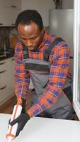 African american worker is applying polyurethane foam to fill gap between sash and window frame. Vertical video