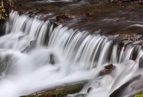 A small waterfall flowing over rocks in a stream photo