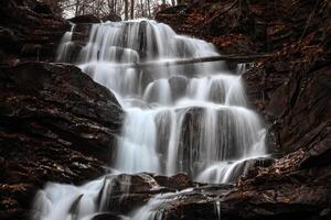 A waterfall in the woods with a large rock photo