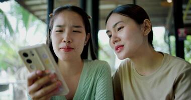 Handheld selective focus shot, Two siblings are playing social media together on smartphone while sitting at a table in a cafe. Family enjoying happy time together. video