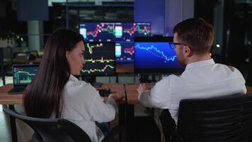 Rear view of traders brokers in formalwear analyzing stock market data while working in dark office video