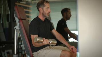 A man engaging in physical exercise at the gym using a dumbbell for his training routine video