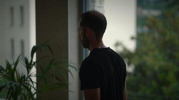A man is holding a fascinating object while sitting near a window in a contemporary, modern setting video