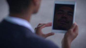 A man is smiling at the reflection of himself on a tablet while in a professional setting video