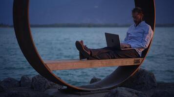 en man är arbetssätt flitigt på hans bärbar dator medan njuter en distinkt kust miljö video