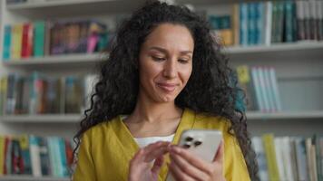 Latin Hispanic Arab woman student mobile phone user smartphone texting sms chatting gadget library university high school college networking smile female girl laugh technology browsing e-learning web video