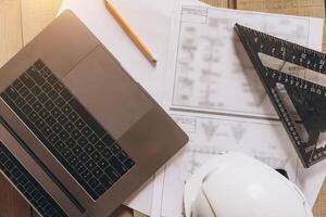Top view mock -up architectural office desk with copy space, wooden floor with laptop, white helmet construction, pencil, ruler and paper roll, copy space, mock up photo