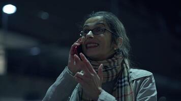 A woman is situated in a bustling nighttime urban setting while using her smartphone device video