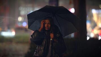 A person is standing in the rain with an umbrella amidst the vibrant city lights at night video
