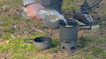 Man in a Hike is Cooking and Pouring Water from the Bottle into the Pot. Traveler in a Forest is Heating Food Using Small Cook Set video