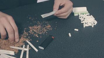 Man in Black Clothing is Rolling a Hand Made Cigarette Using Papers, Filters and Tobacco. A Way to Save on Tobacco Products. Tobacco Product Economy Concept. Top View video