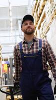 Warehouse worker is working with hand pallet truck or pallet jack and cargo pallet in a construction store in tile section. Vertical video