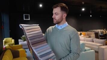 A man choosing upholstery fabric color and texture from various colorful samples for sofa in a store video