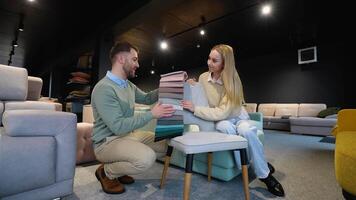 A man and woman choosing upholstery fabric color and texture from various colorful samples for armchair in a store video