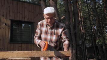 A senior craftsman focuses on cutting wood with precision while surrounded by lush trees under a bright afternoon sun. The tranquility of nature enhances the moment. video