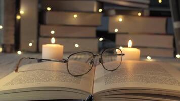 Flickering candles provide soft light over an open book, while a pair of Eyeglasses rests on the pages, creating a tranquil reading atmosphere on a calm evening. video