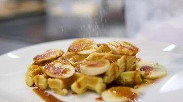 Sprinkle waffles with banana and caramel with powdered sugar soft Belgian waffles served on plate, pile of fluffy waffles garnished with fresh berries place on wooden table video