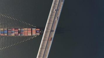 The container ship passes under a large bridge over which cars are moving video