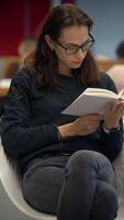 uma mulher é profundamente absorta dentro lendo uma livro enquanto sentado dentro uma à moda moderno espaço video