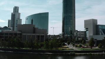 View of the metropolis from a height. Stock footage. Sunny landscape on tall buildings made of glass and parks around the river on the background of blue sky. video