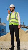 Foreman instructing workers using walkie talkie radio set at quarry. Vertical video