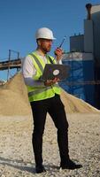 Foreman with laptop instructing workers using walkie talkie radio set at quarry. Vertical video