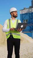 Engineer in hardhat use laptop to plan the work of a quarry. Vertical video