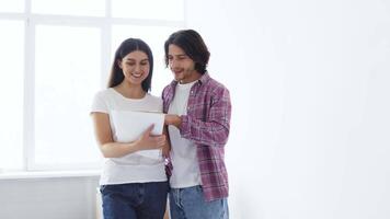 A young couple stands in a bright, minimalist space, sharing ideas as they look at a notebook. The woman smiles while the man points at the notes, both engaged and happy. video