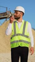 Foreman instructing workers using walkie talkie radio set at quarry. Vertical video