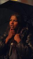 A young person in deep thought, sheltered by an umbrella, is illuminated by soft dim lighting video