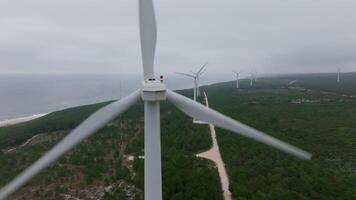 Several wind turbines in a row above a green forest, road visible below, cloudy sky overhead video