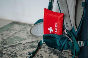 A bright red first aid kit is attached to a worn backpack, suggesting its for hiking or outdoor adventures, highlighting the importance of being prepared for emergencies photo
