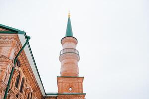 There is a brick building that features a green tower situated at the very top of its structure, creating a striking and memorable visual that stands out remarkably in the surrounding area photo
