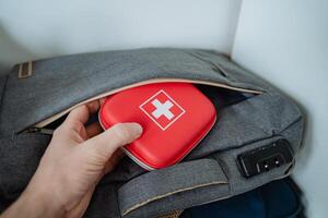 A person is carefully placing a first aid kit into a backpack, ensuring that it is secure and easily accessible for emergencies, while also organizing their luggage effectively photo