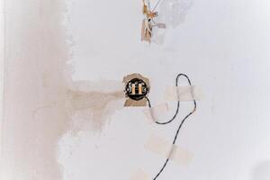 There is a white wall that features a significant hole in it, from which a wire is protruding, suggesting possible electrical work or modifications might have taken place photo