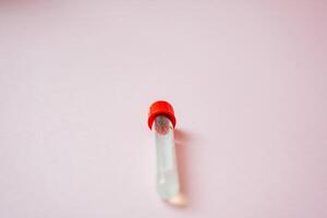 A test tube that features a bright red cap is carefully placed on a soft pink surface, highlighting its vibrant color beautifully, while it creates a striking contrast with the background photo