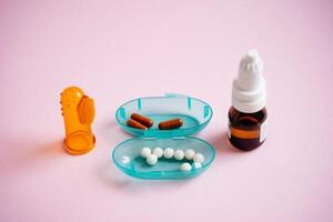 A vibrant blue container that is filled to the brim with various pills, alongside a bottle of liquid drops, all positioned on a striking pink surface, creating a visually appealing scene photo