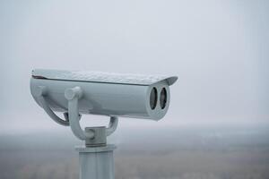 A security camera, positioned on a tall pole, diligently oversees the area below, while the thick fog heavily impairs visibility, creating significant challenges in seeing clearly photo