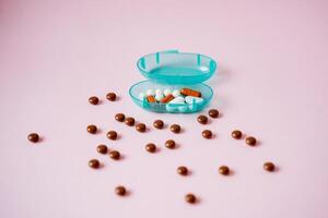On a vibrant pink surface, there lies a blue container that is packed with an assortment of pills and brown balls, creating an intriguing display of various substances altogether photo
