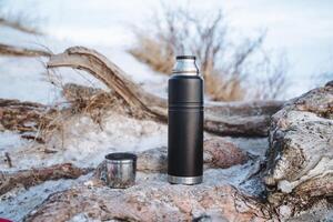 A sleek black thermos is perfectly positioned on top of a textured pile of rocks, showcasing its stylish design and practicality. It is ready to hold your favorite beverage photo