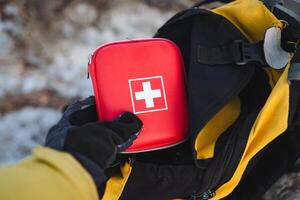 A person is carefully placing a first aid kit into their backpack, ensuring that they have all necessary supplies for any potential emergencies while enjoying their outdoor activities photo