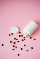 A large white bottle, packed with an array of colorful pills, precariously leans against a vibrant pink background. This tilt creates a striking, attentiongrabbing cascade of pills photo
