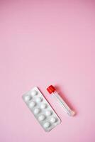 On a light pink background, there is a bright, vibrant blister pack filled with pills accompanied by a test tube, creating an appealing visual relevant to healthcare and medicine photo