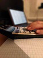 Close-up of female hand using calculator with laptop in office setting photo